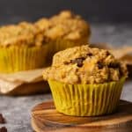 A muffin on a concrete bench next to two more muffins on a wooden cutting board. Moody light.