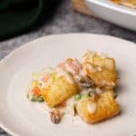 A serving of seafood pie on a white plate next to the casserole dish.