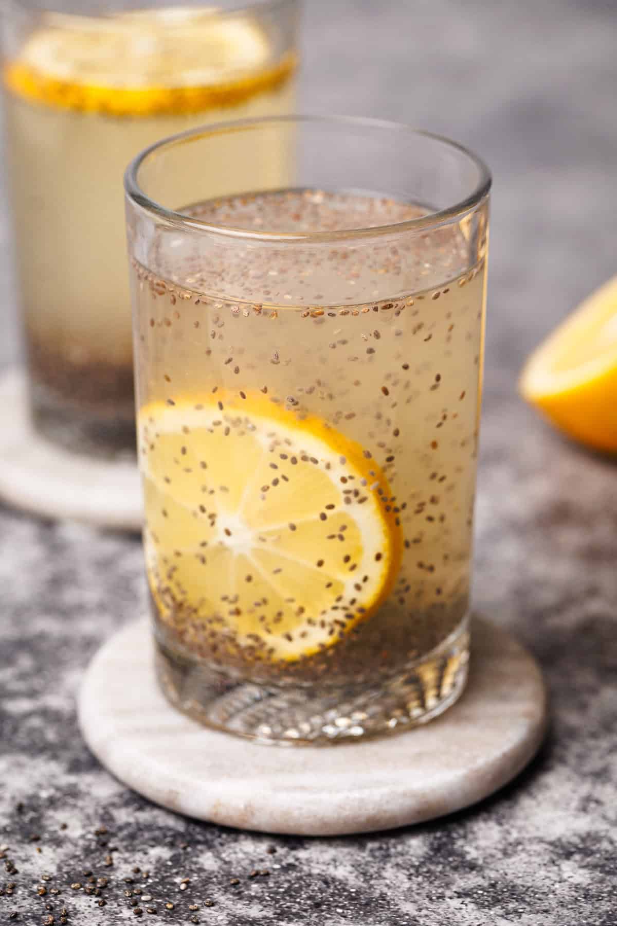 Two glasses with chia lemonade on marble coasters next to half a lemon.