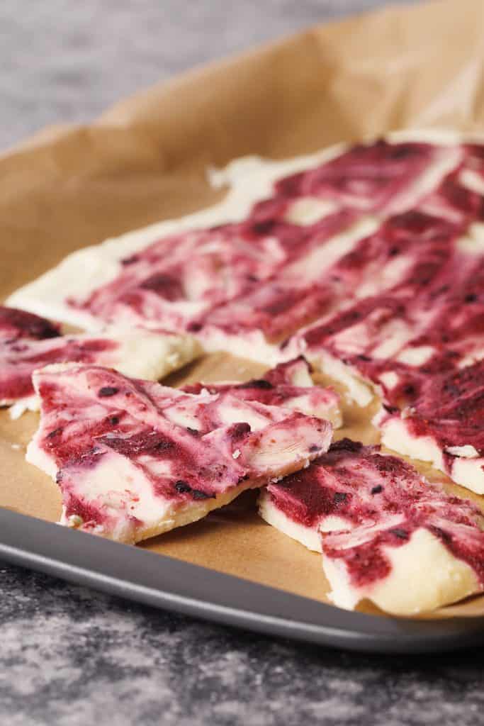 Frozen yogurt bark with berries on a baking sheet broken into pieces.