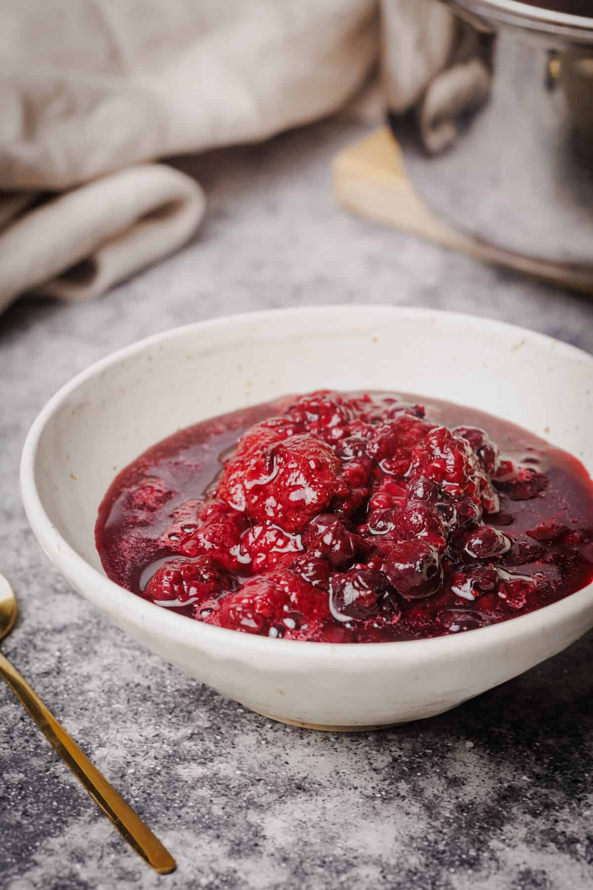 Stewed berries in a cream bowl next to a tea towel and saucepan.