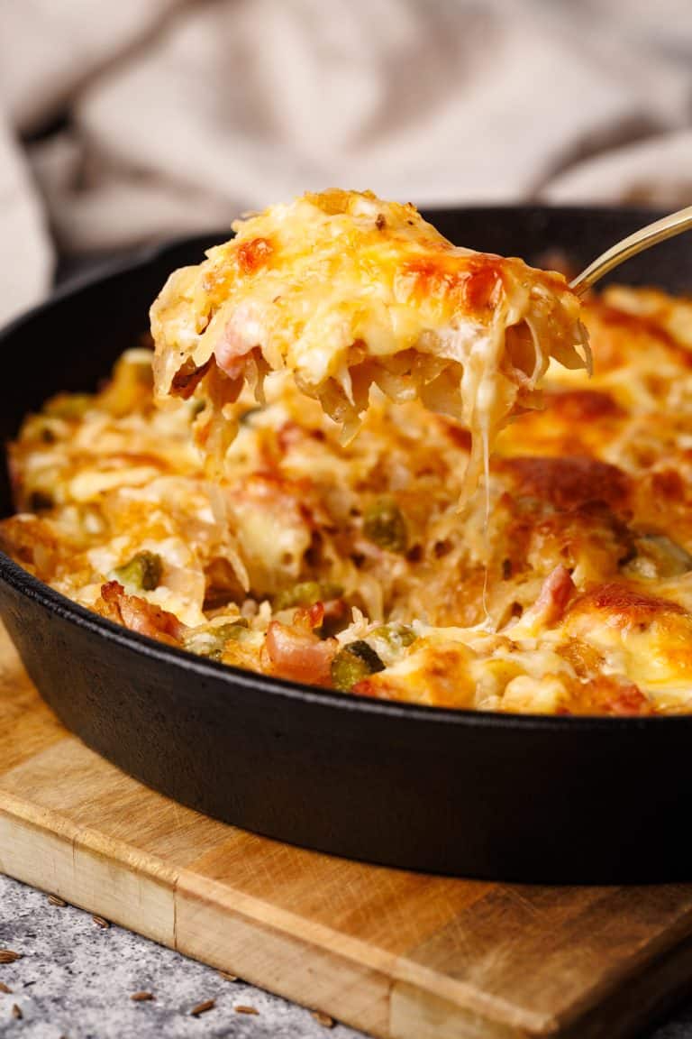 Sauerkraut casserole being scooped out of a cast iron skillet.