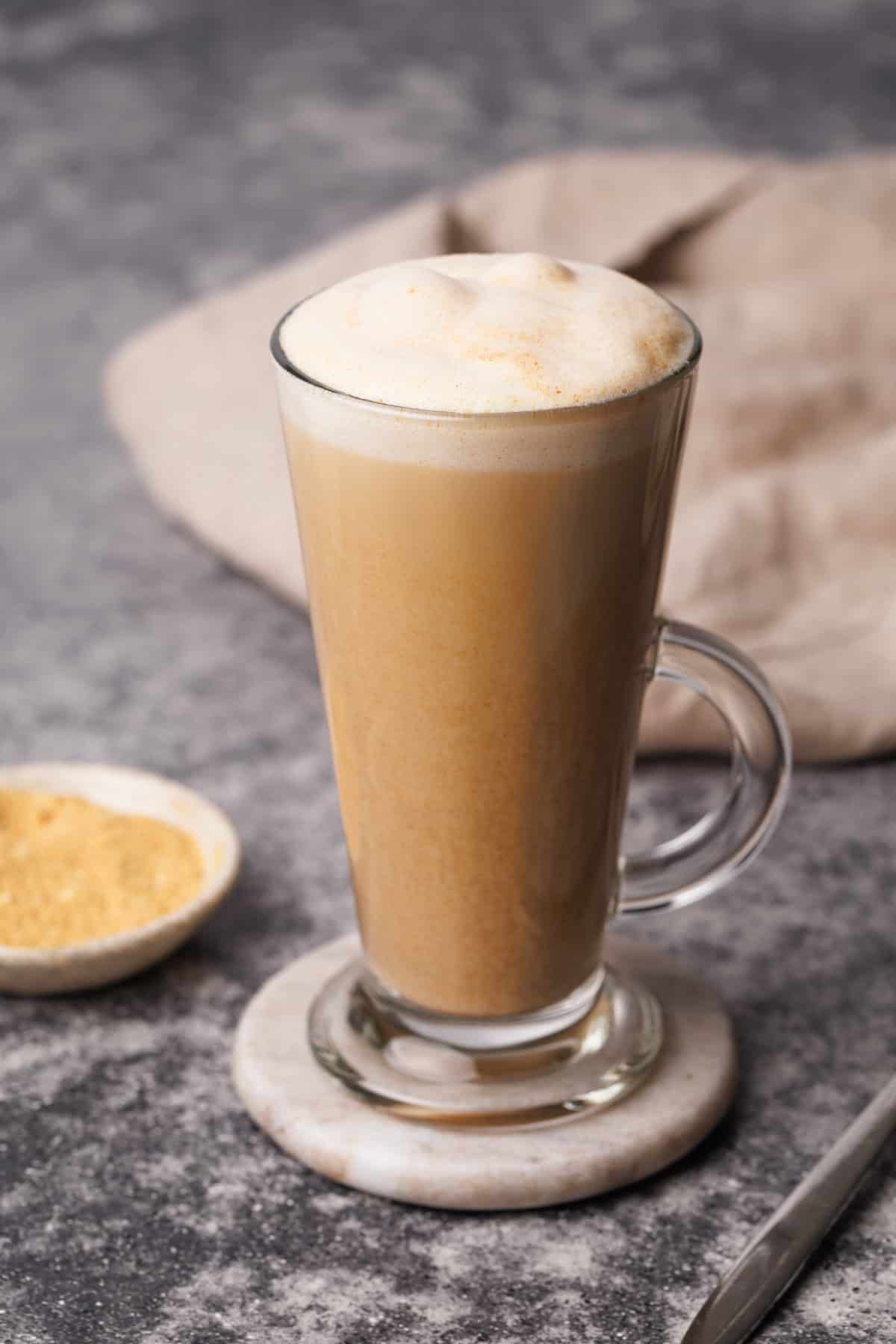 Latte in a tall glass cup on a marble coaster next to toasted milk and a napkin.