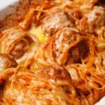 Spaghetti and meatballs baked in a white casserole dish, covered with melted cheese.
