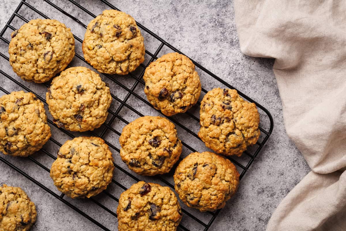 Oatmeal cookies on a cooling rack next to linen towel.