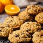 Oatmeal cookies on a cooling rack next to linen towel.