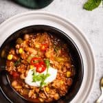 A serving of chili in a black bowl next to the Dutch oven.