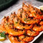 Cooked tiger shrimp on a white plate next to a lemon and parsley.