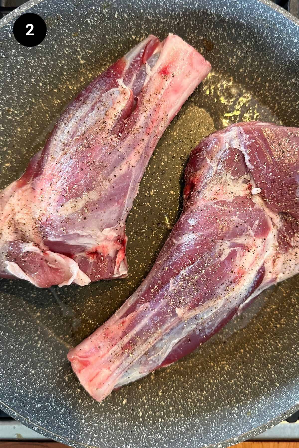 Lamb shanks being seared in a pan.