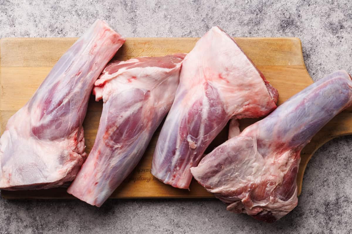 Uncooked lamb shanks on a wooden board.