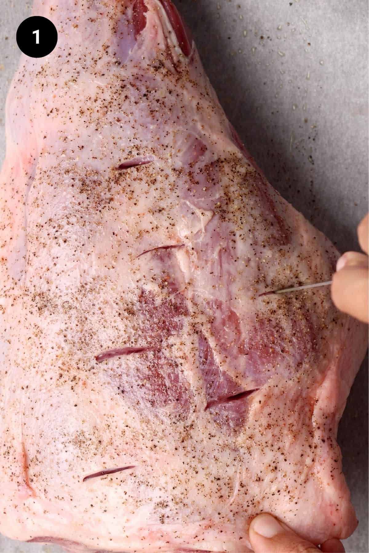 Seasoned lamb leg being pierced with a small knife.