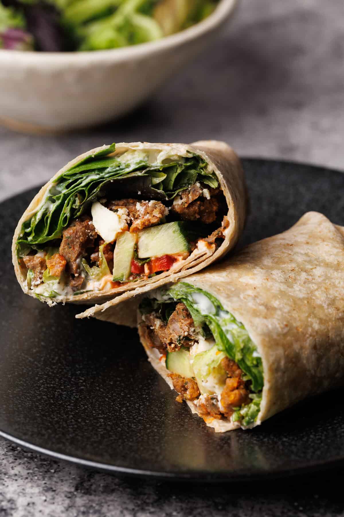 A lamb wrap cut in half on a black plate.