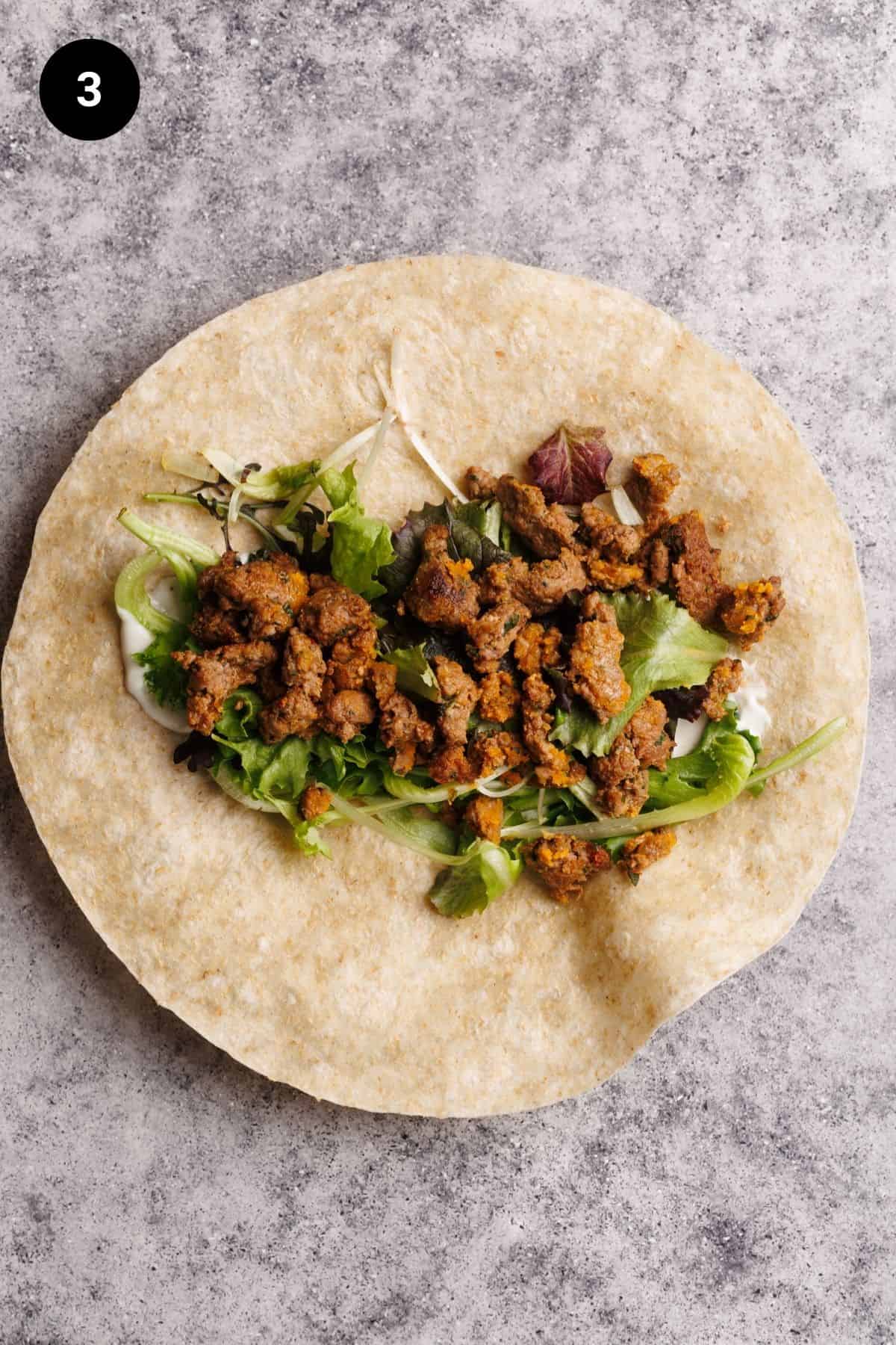 Salad and cooked sausage on a flour tortilla.