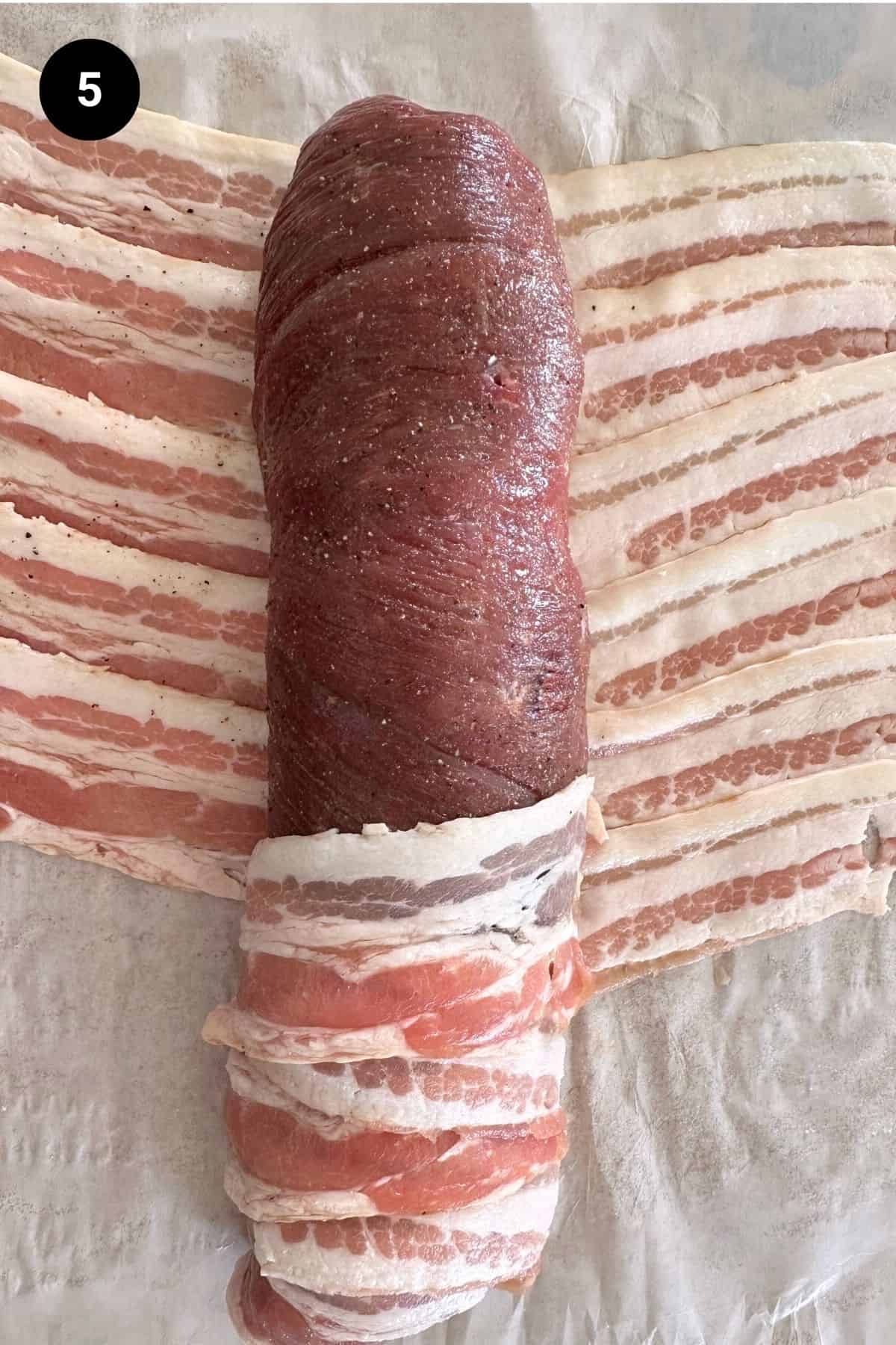 Stuffed lamb leg being wrapped in bacon.