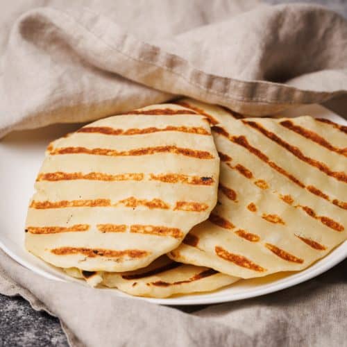 Flatbreads on a white plate covered in a natural linen tea towel.