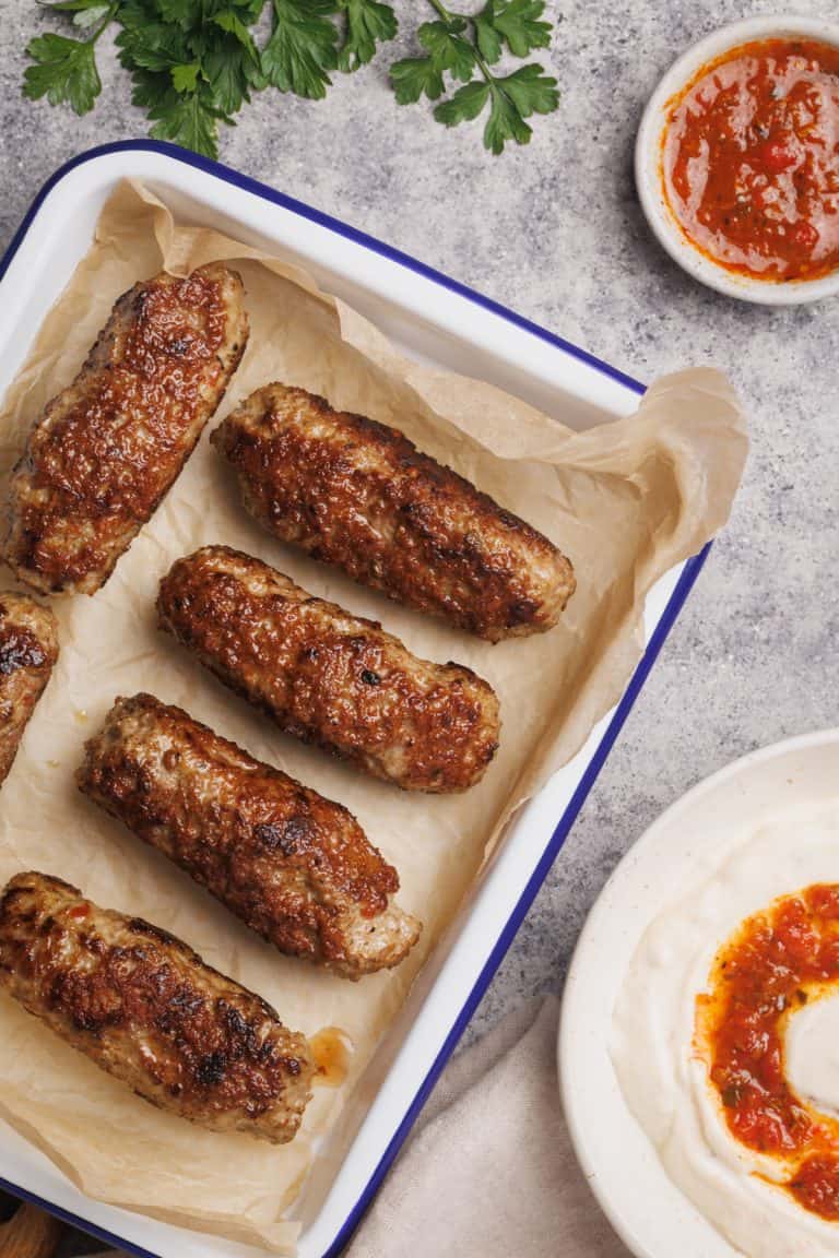 An enamel tray with lamb sausages next to dips.