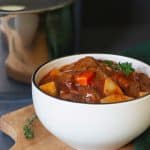 Beef stew in a small white bowl next to a large pot.