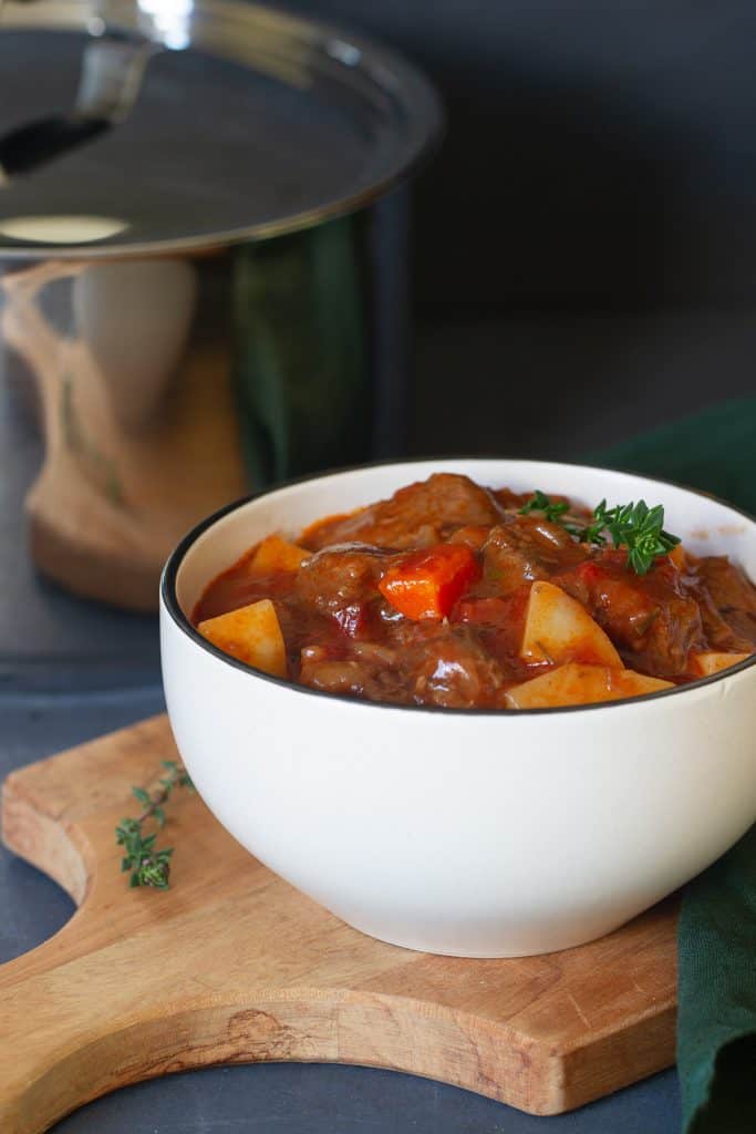 Beef stew in a small white bowl next to a large pot.