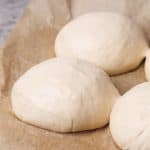 Three pizza dough ball on brown baking paper.