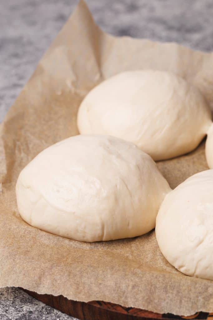 Three pizza dough ball on brown baking paper.
