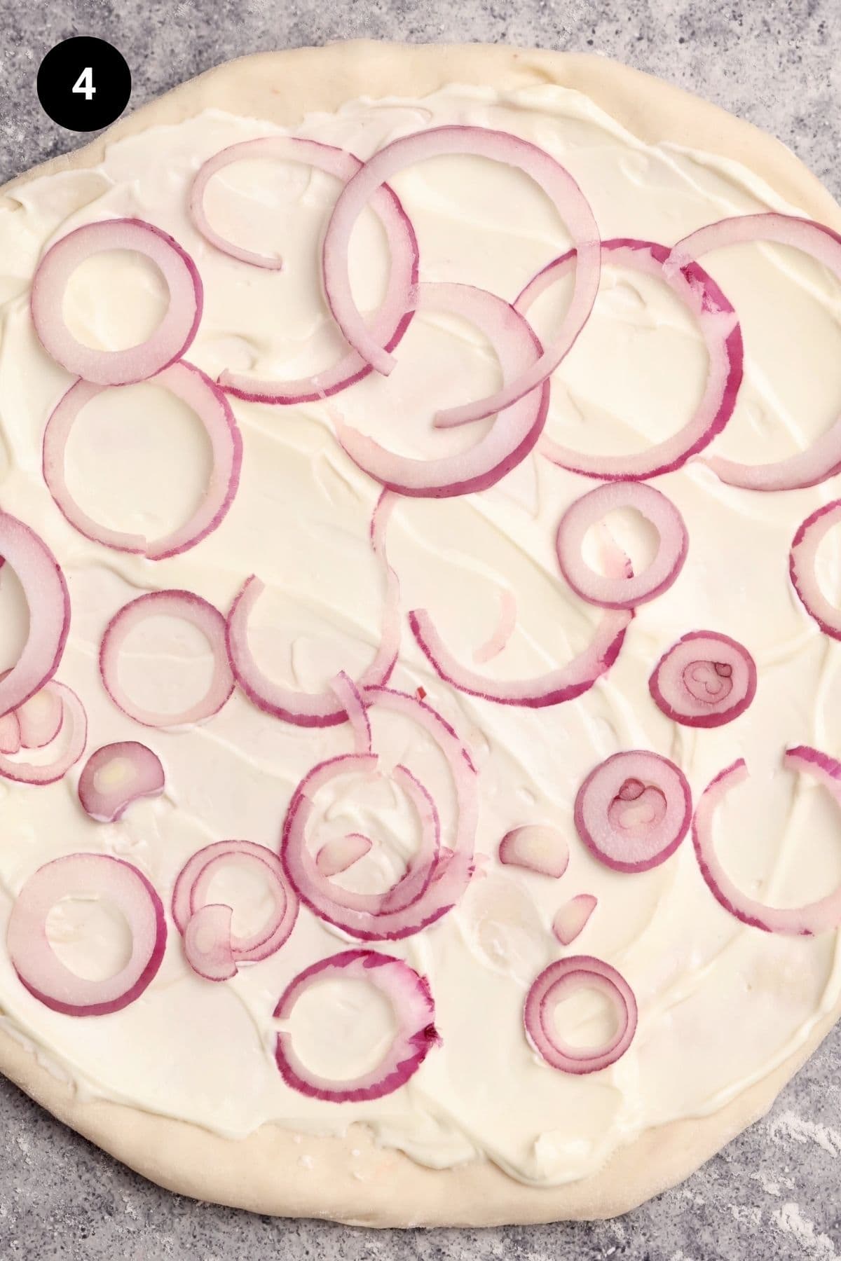 Pizza dough with sour cream and red onion slices.