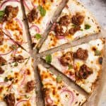 Sliced German pizza on a baking paper lined wooden board next to a linen napkin.