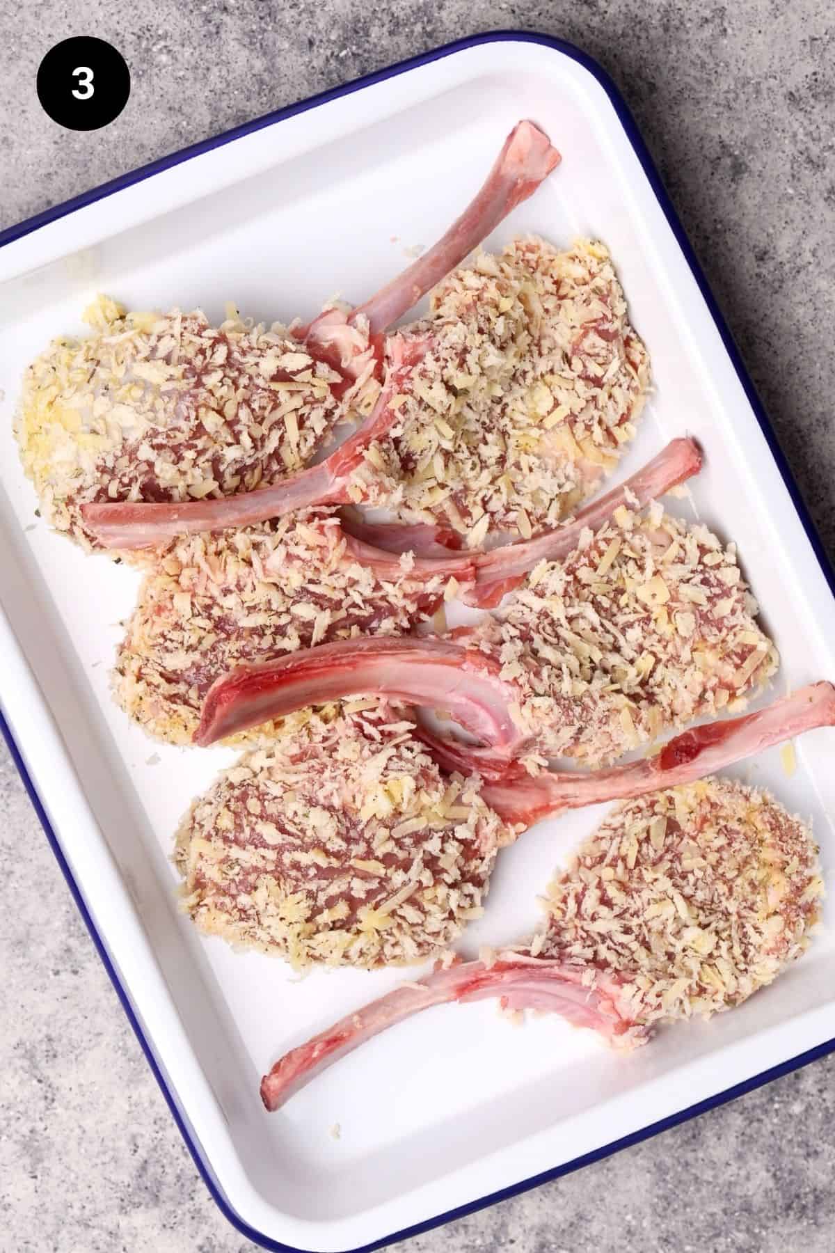 Crumbed lamb chops on a white tray before being fried.