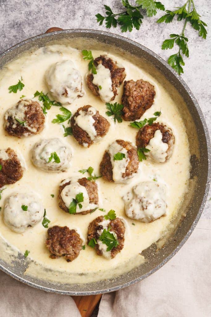 Alfredo sauce with meatballs in a large pan next to some fresh parsley on a concrete background.