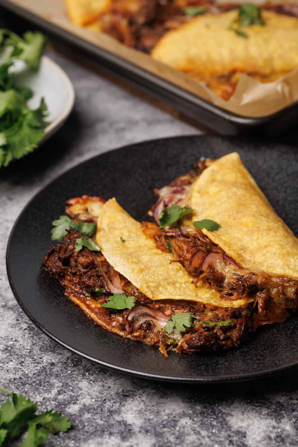 Two baked birria tacos on a black plate.