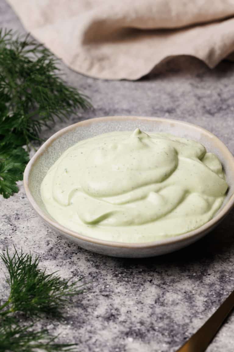Ranch dip in a small bowl next to fresh herbs and a linen tea towel.