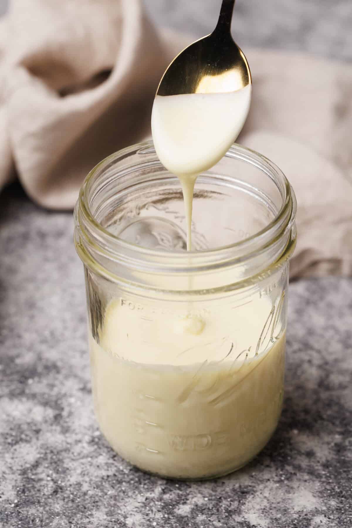 A mason jar with evaporated milk and a spoon spooning it out.