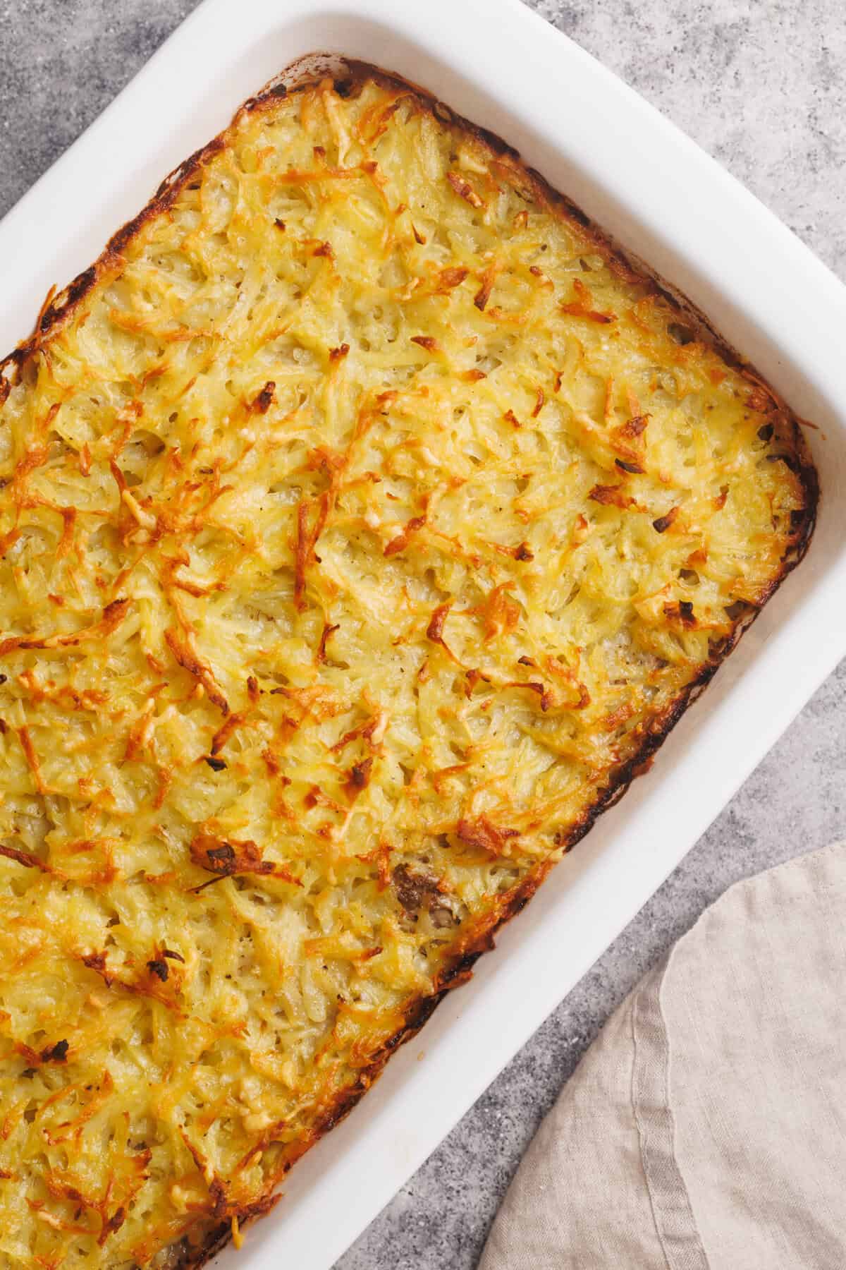 Hash brown beef casserole in a white casserole dish next to a linen towel.