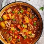 A Dutch oven filled with Hungarian goulash next to parsley.