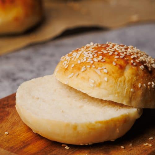 Hamburger bun cut in half on a wooden board.