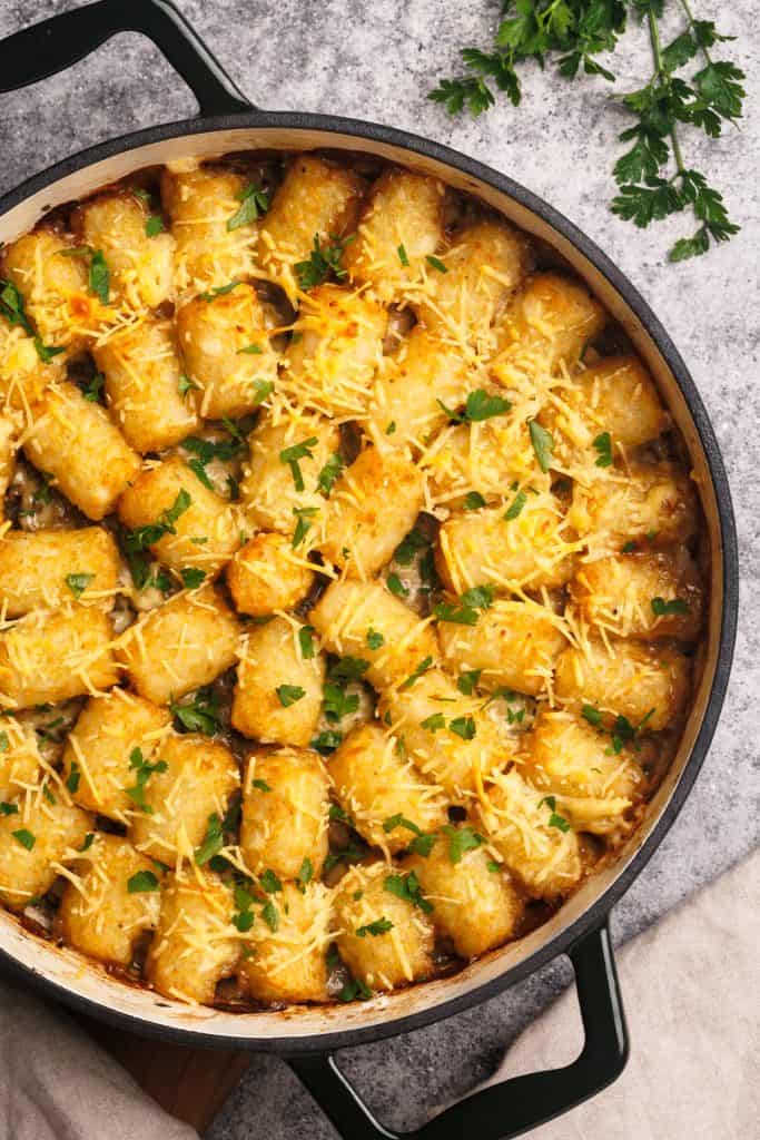 Top down view of the tater tot casserole next to a linen tea towel and fresh parsley.
