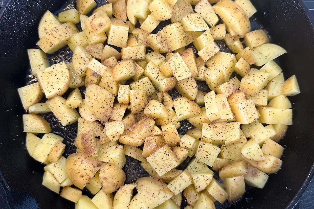 Potato pieces being fried in a cast iron pan.