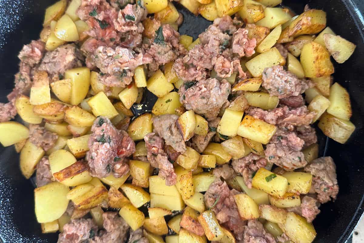 Sausage and potatoes being fried in a cast iron pan.
