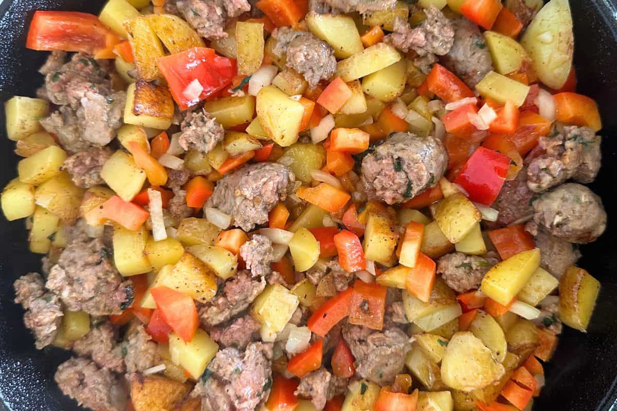 Vegetables, sausage, and potatoes being fried in a cast iron pan.