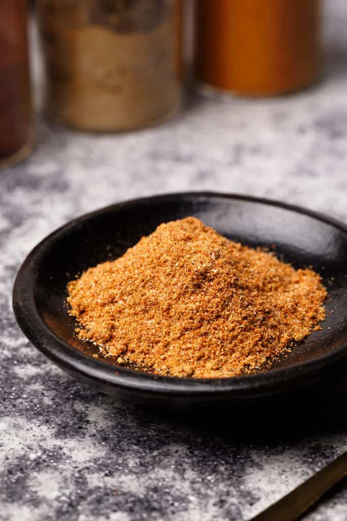 Shawarma spice mix in a black wooden dish next to spice jars.