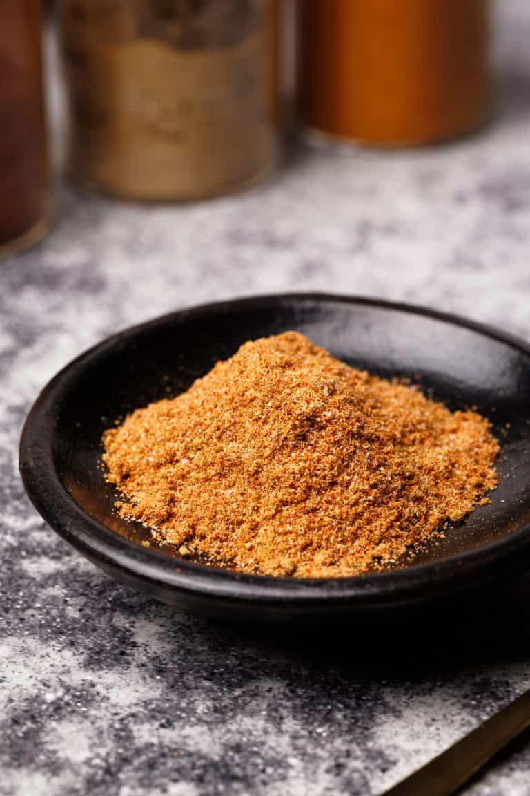 Shawarma spice mix in a black wooden dish next to spice jars.