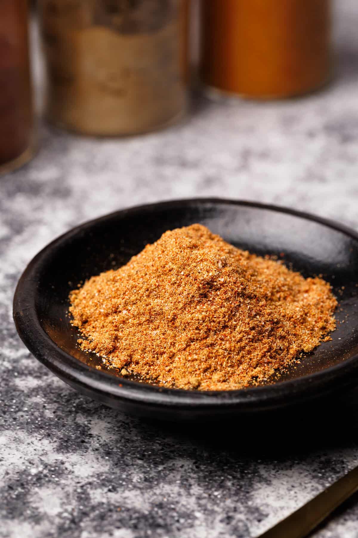 Shawarma spice mix in a black wooden dish next to spice jars.