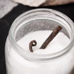 A mason jar filled with sugar with a vanilla bean sticking out.
