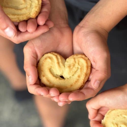 A child's hand holding a spritz cookie.