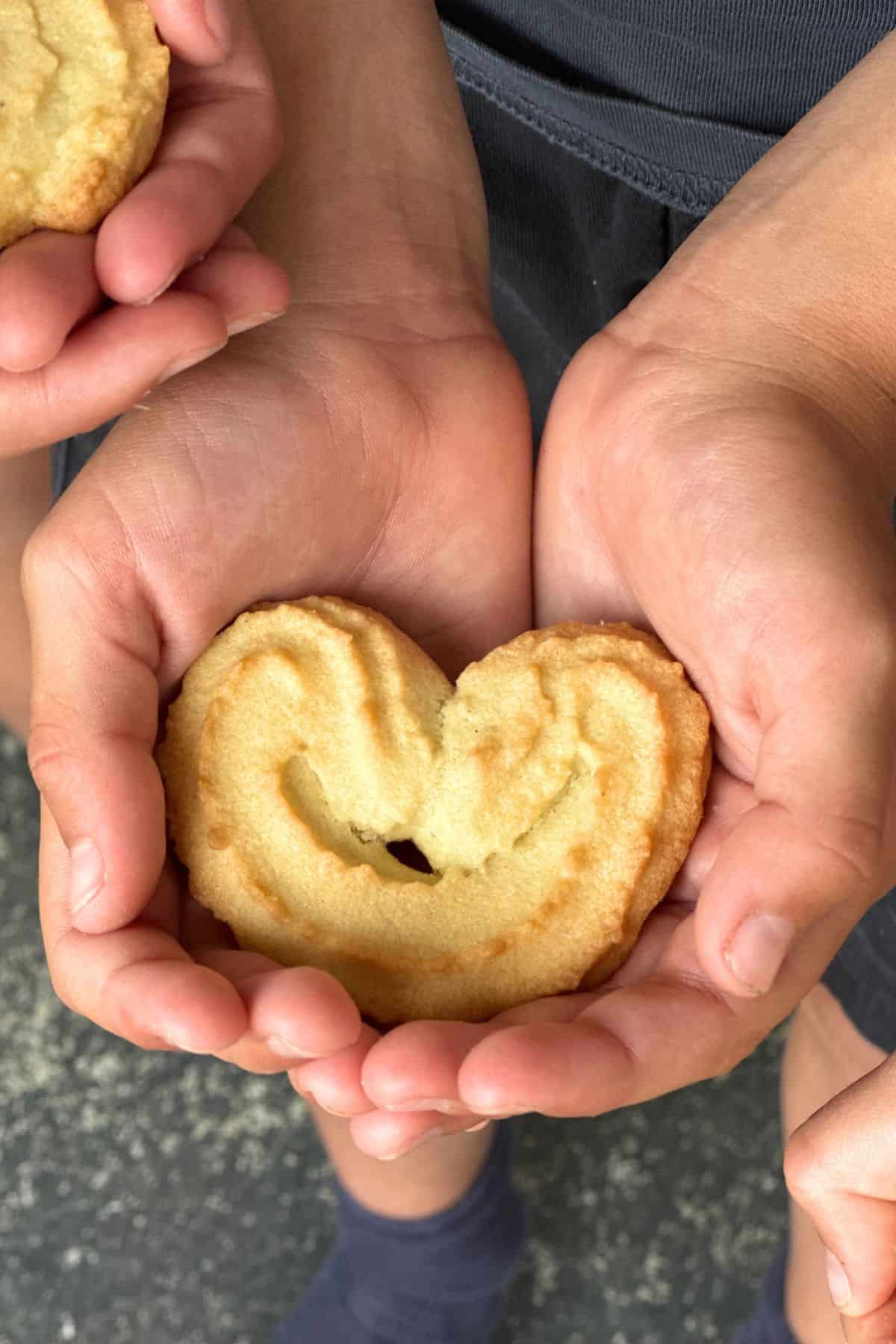 A child's hand holding a spritz cookie.