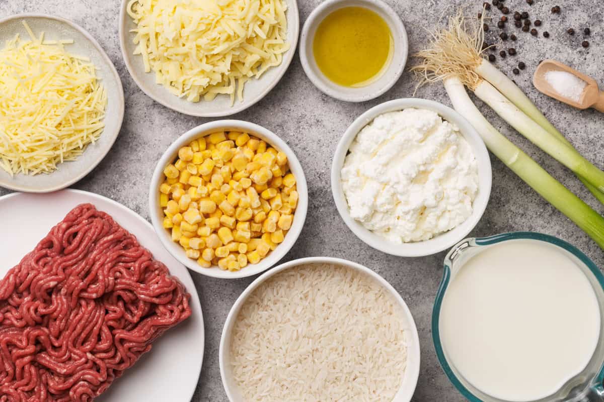 Fresh ingredients for cheese and beef recipes, including shredded cheese, ground beef, corn, and mil.