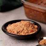 Barbacoa spice mix in a black bowl next to a container of barbacoa.