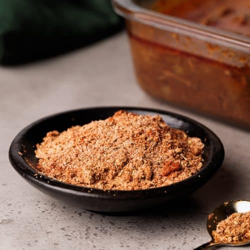 Barbacoa spice mix in a black bowl next to a container of barbacoa.