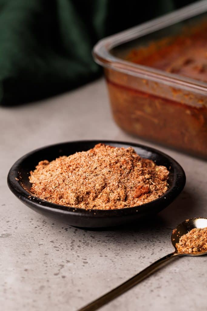 Barbacoa spice mix in a black bowl next to a container of barbacoa.
