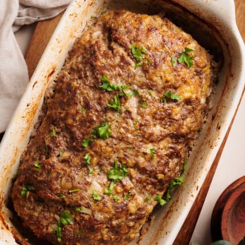 Cottage Cheese Meatloaf in a ceramic loaf pan on a wooden board.
