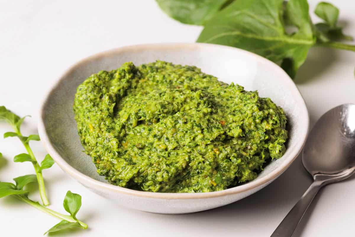 Watercress pesto in a small bowl next to watercress and a silve spoon.